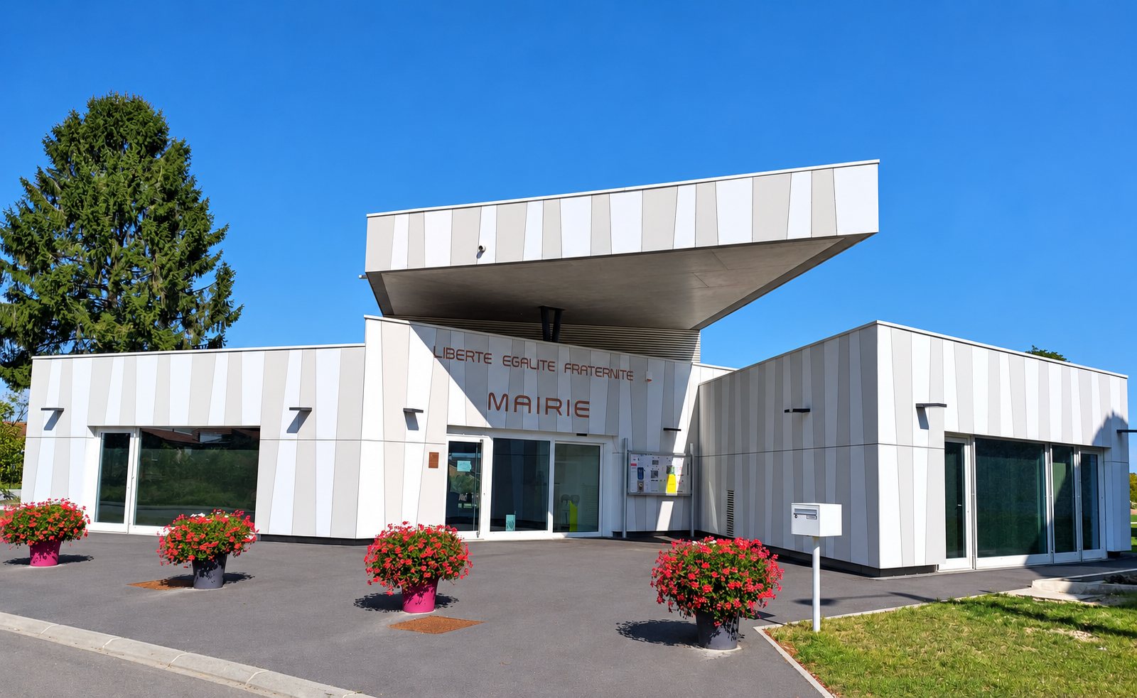 La mairie de Morfontaine, bâtiment moderne à façade blanche et grise avec auvent, jardinières fleuries